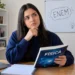 Estudante pensativa com livro de Física em quarto de estudos.