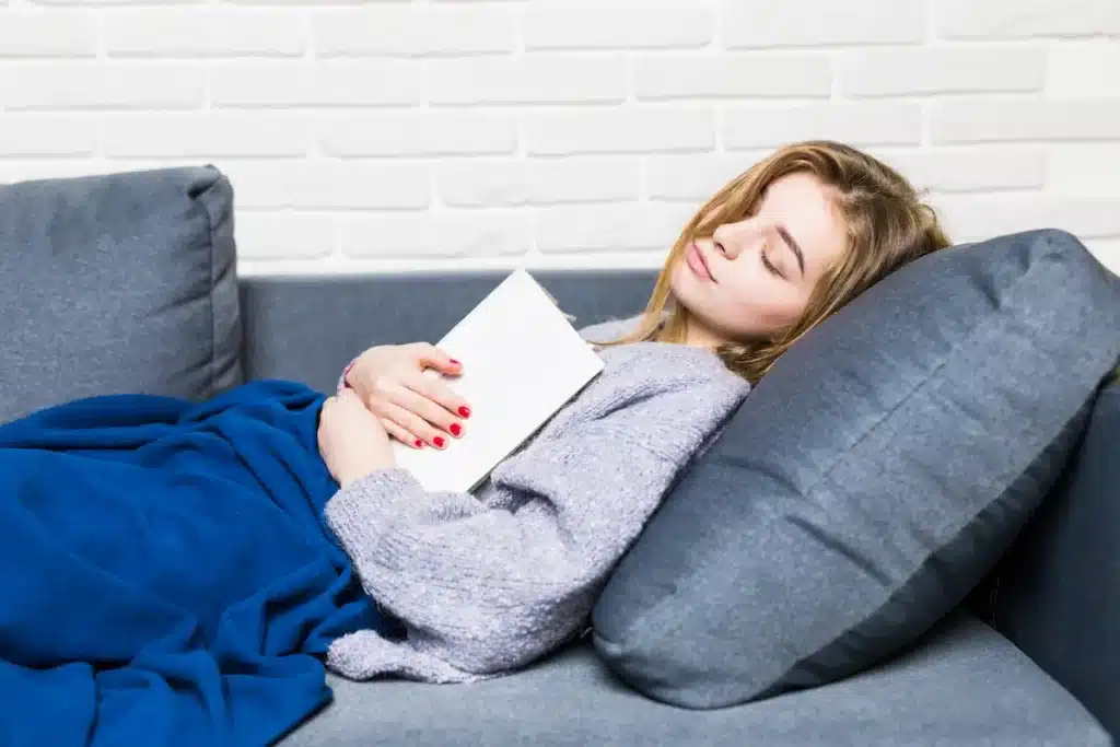 Jovem descansando no sofá com livro nas mãos em ambiente aconchegante.