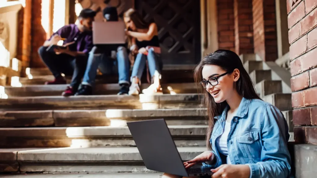 Jovens estudam juntos nas escadarias de uma universidade com notebooks.