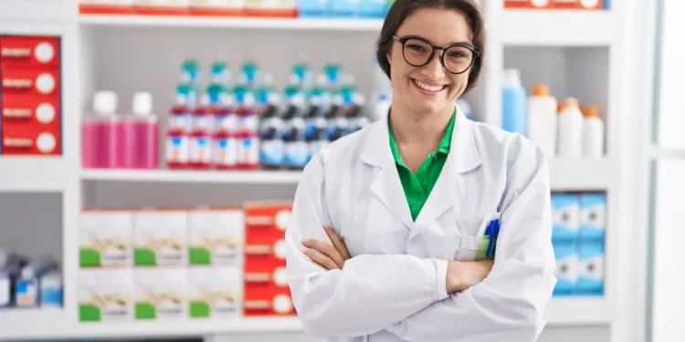 Farmacêutica sorridente em farmácia moderna com jaleco branco.