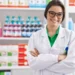 Farmacêutica sorridente em farmácia moderna com jaleco branco.