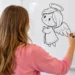 Jovem desenha um anjo no quadro branco em ambiente claro.