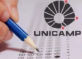 Mão segurando lápis azul preenche cartão-resposta ao lado do logotipo da Unicamp.