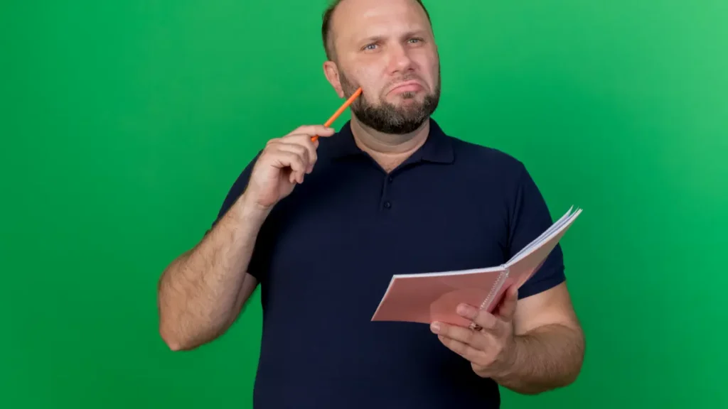 Homem segurando caderno e lápis em fundo verde.