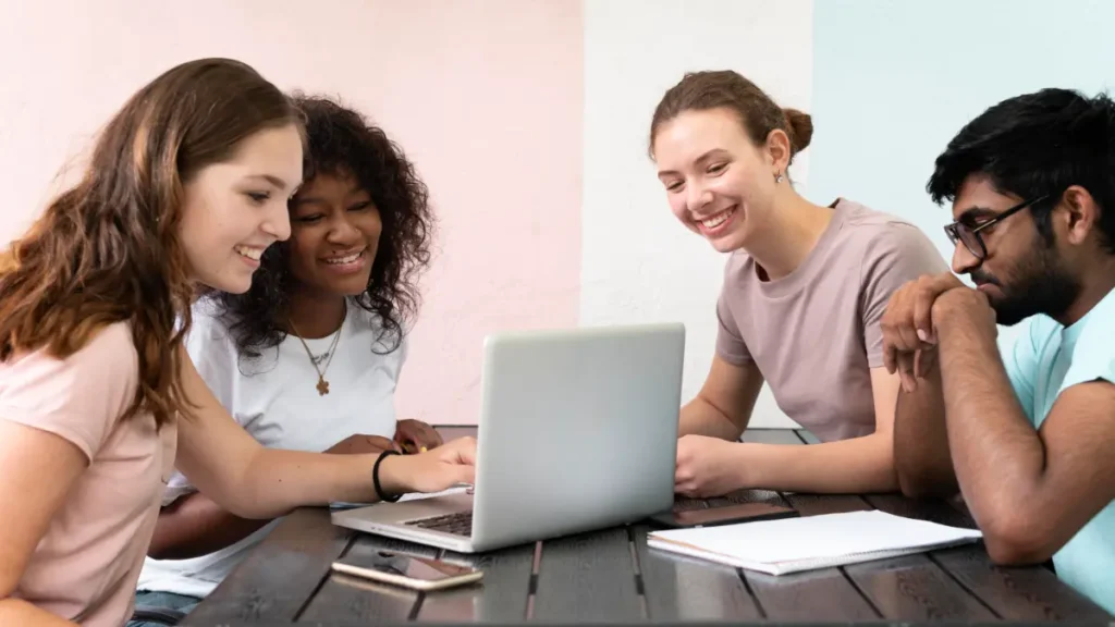 Jovens estudantes colaborando em grupo ao redor de notebook.