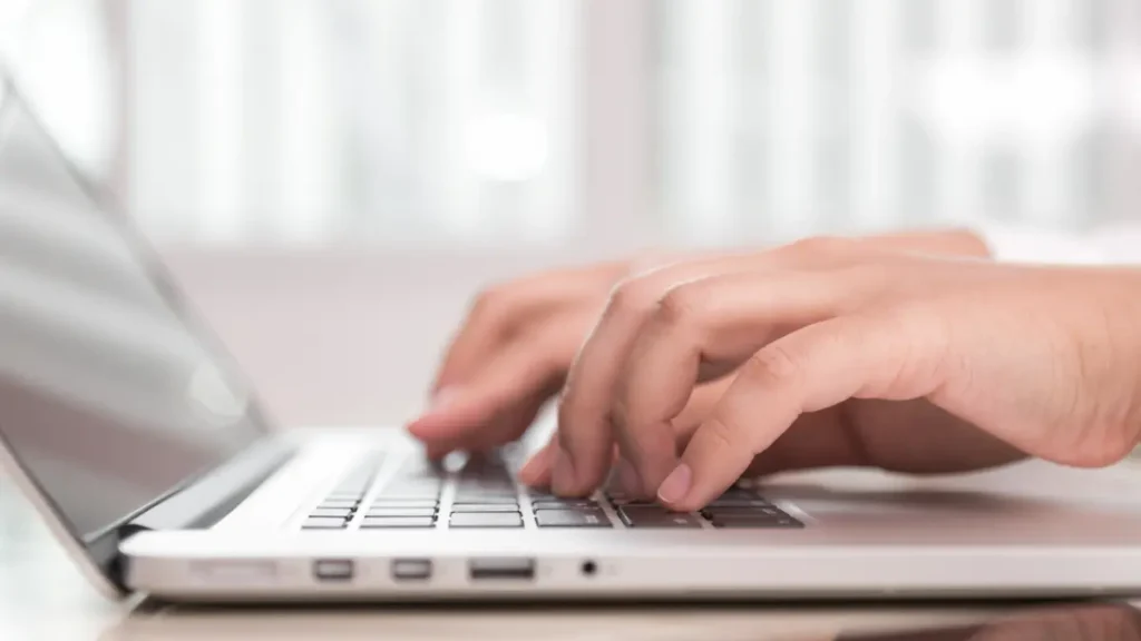 Mãos femininas teclando em notebook, realizando inscrição no Enem/USP 2027.