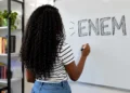 Jovem escrevendo o nome Enem em quadro branco.