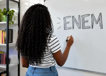 Jovem escrevendo o nome Enem em quadro branco.