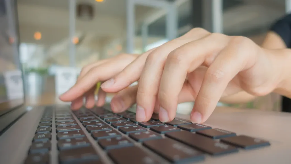 Mãos digitando inscrição online em notebook para pós-graduação UFGD.