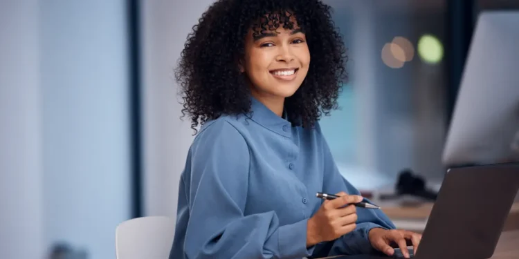 Jovem profissional negra sorrindo enquanto trabalha em escritório moderno.