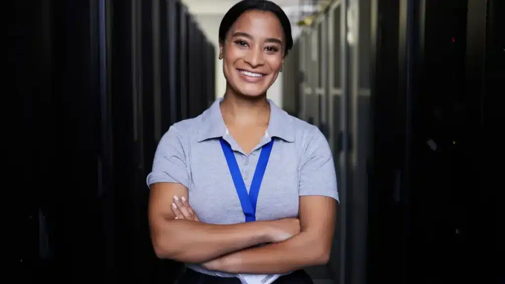 Profissional de TI sorridente em data center reforça diversidade no trabalho.