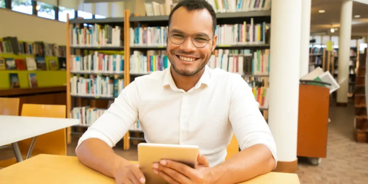 Jovem sorridente usando tablet em biblioteca moderna.