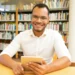 Jovem sorridente usando tablet em biblioteca moderna.