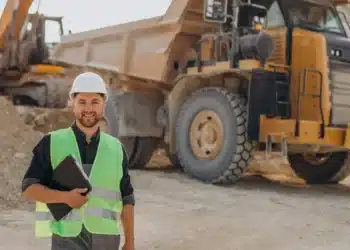 Homem em mineração com equipamentos pesados e caminhão basculante em obra.