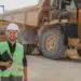 Homem em mineração com equipamentos pesados e caminhão basculante em obra.