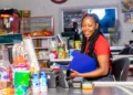 Atendente sorridente em caixa de mercado moderno com doces e produtos.