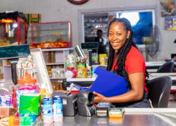 Atendente sorridente em caixa de mercado moderno com doces e produtos.
