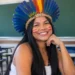 Mulher indígena com cocar de penas e pinturas vermelhas no rosto sentada em uma sala de aula, em referência à pós-graduação indígena.