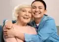 Jovem abraça idosa sorridente em momento de carinho no sofá.