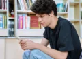 Jovem mexendo no celular em biblioteca.