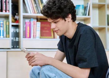 Jovem mexendo no celular em biblioteca.