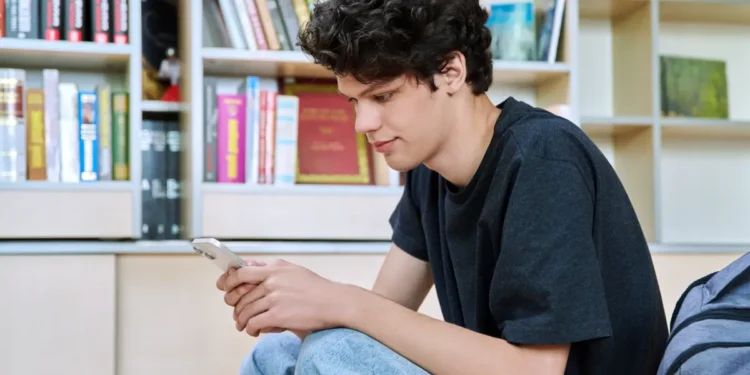 Jovem mexendo no celular em biblioteca.