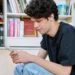 Jovem mexendo no celular em biblioteca.