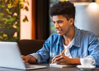 Jovem estudando em cafeteria com notebook e caderno aberto.
