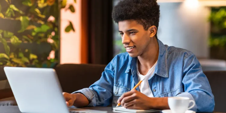 Jovem estudando em cafeteria com notebook e caderno aberto.