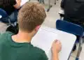 Jovem realiza prova de Linguagens em sala de aula iluminada.