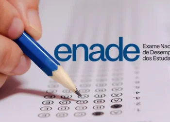 Mão preenche questão de múltipla escolha de prova do Enade com lápis azul ao lado do logo do exame.