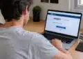 Jovem com manchas vermelhas no corpo, olhando para página do Enem no notebook.