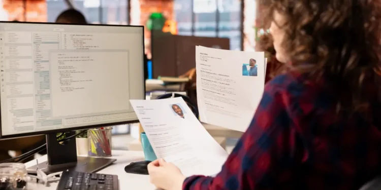 Análise de currículos por recrutadora em ambiente de escritório moderno.