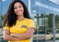 Jovem aprendiz sorridente em frente à indústria de vidros.