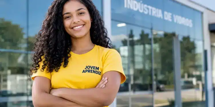 Jovem aprendiz sorridente em frente à indústria de vidros.