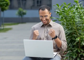 Homem feliz comemora inscrição em especialização da UFGD ao ar livre.