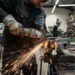 Profissional utiliza esmerilhadeira em bancada de serralheria industrial.