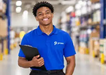 Jovem negro com camisa azul da Praso e prancheta, em um depósito.