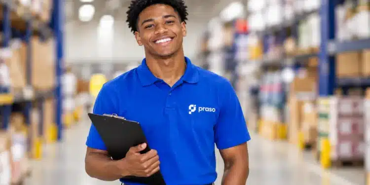 Jovem negro com camisa azul da Praso e prancheta, em um depósito.