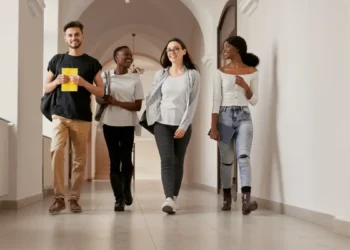 Jovens estudantes caminhando sorridentes no corredor de faculdade.