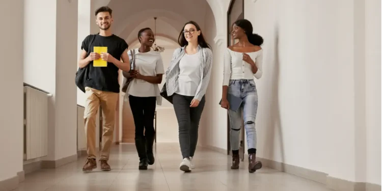 Jovens estudantes caminhando sorridentes no corredor de faculdade.