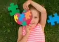 Criança sorrindo segura coração de peças coloridas símbolo do autismo.
