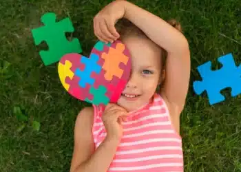Criança sorrindo segura coração de peças coloridas símbolo do autismo.