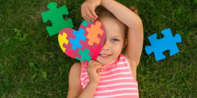 Criança sorrindo segura coração de peças coloridas símbolo do autismo.