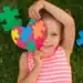 Criança sorrindo segura coração de peças coloridas símbolo do autismo.