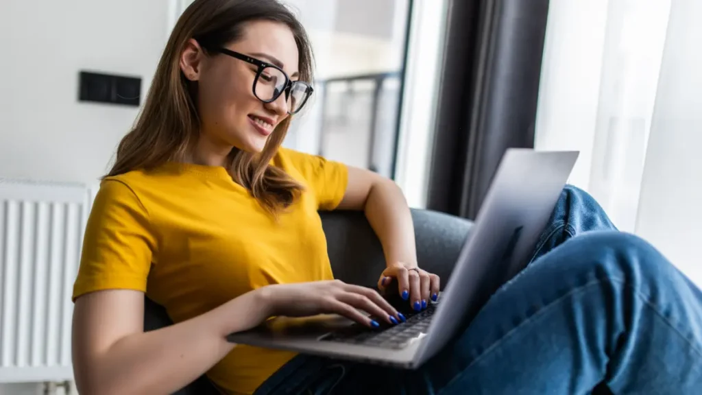 Jovem sorridente usando notebook em ambiente doméstico iluminado.