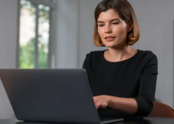 Jovem digitando em notebook em escritório.