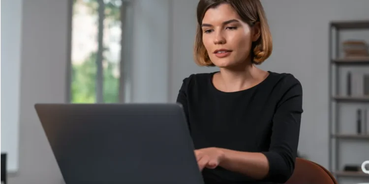Jovem digitando em notebook em escritório.