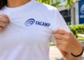 Pessoa segura camiseta branca com o logotipo da Facamp em área externa iluminada.