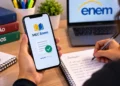 Jovem acessando app MEC Enem no celular, rodeada de livros, anotações e notebook com ENEM 2026 na tela, simbolizando o app MEC Enem.